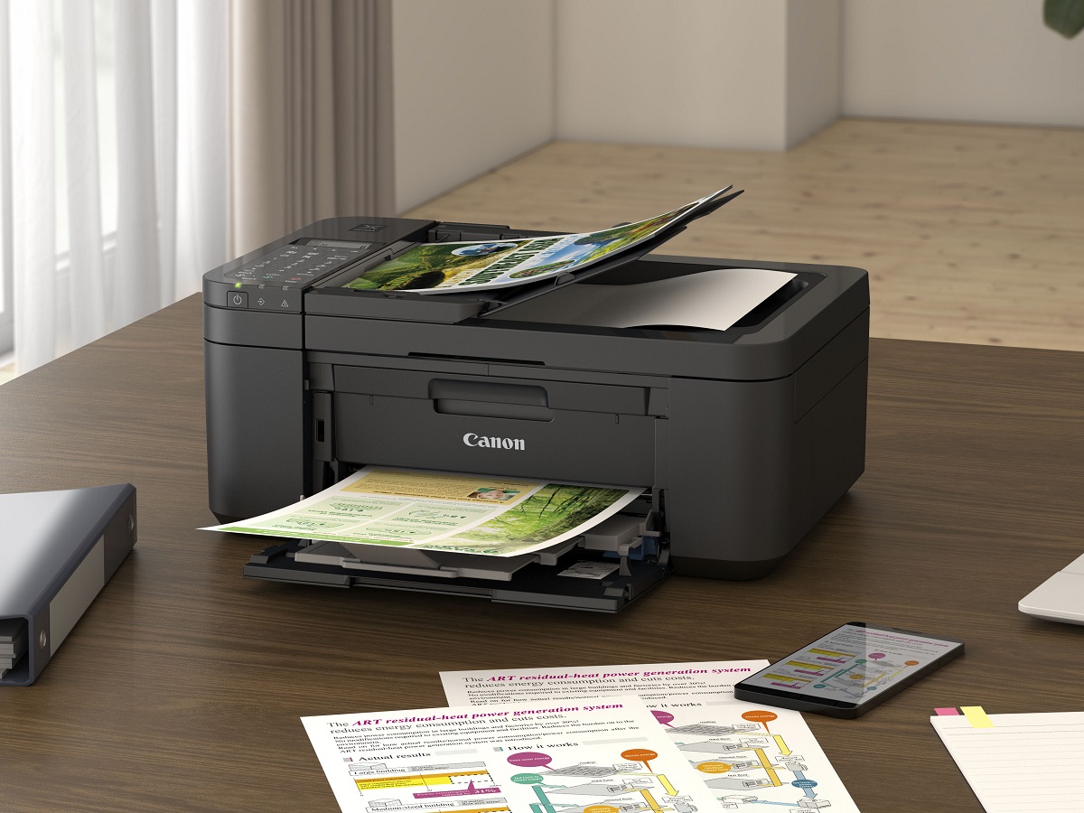 A impressora a jato de tinta multifuncional sem fio Canon PIXMA TR4720 em uma mesa, imprimindo páginas.