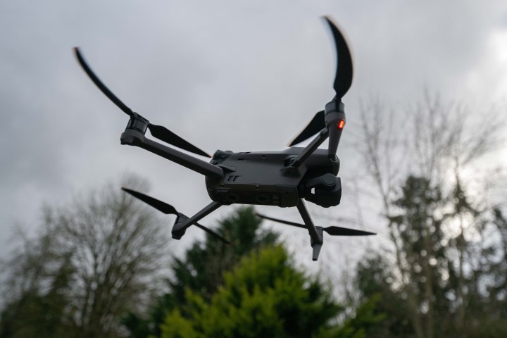 The DJI Mavic 3 Classic flying beneath a cloudy sky with trees.