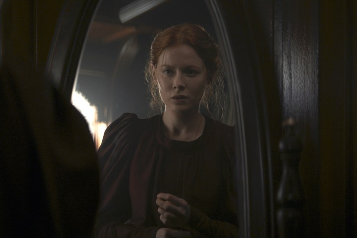 Emily Beecham stands in front of a mirror in 1899.