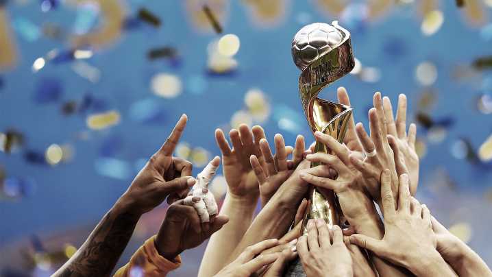 The FIFA World Cup trophy held aloft by a group of hands.