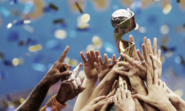 The FIFA World Cup trophy held aloft by a group of hands.