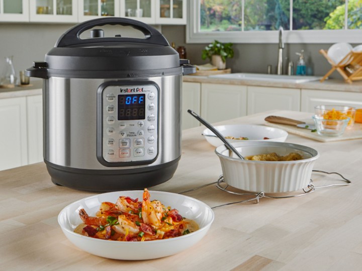 Instant Pot 6-quart Duo Plus 9-in-1 Electric Pressure Cooker on a wooden counter with a cooked shrimp dish.