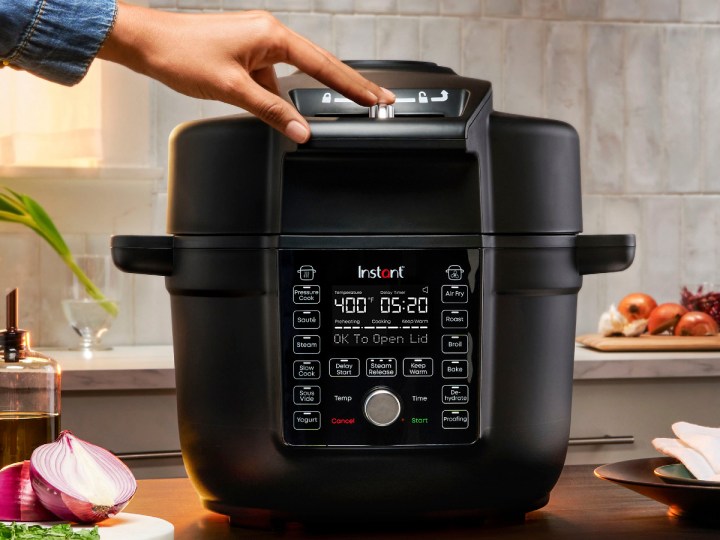 Instant Pot 6.5-quart Duo Crisp with Ultimate Lid Multi-Cooker + Air Fryer with a man's hand sliding the lid unlock button.