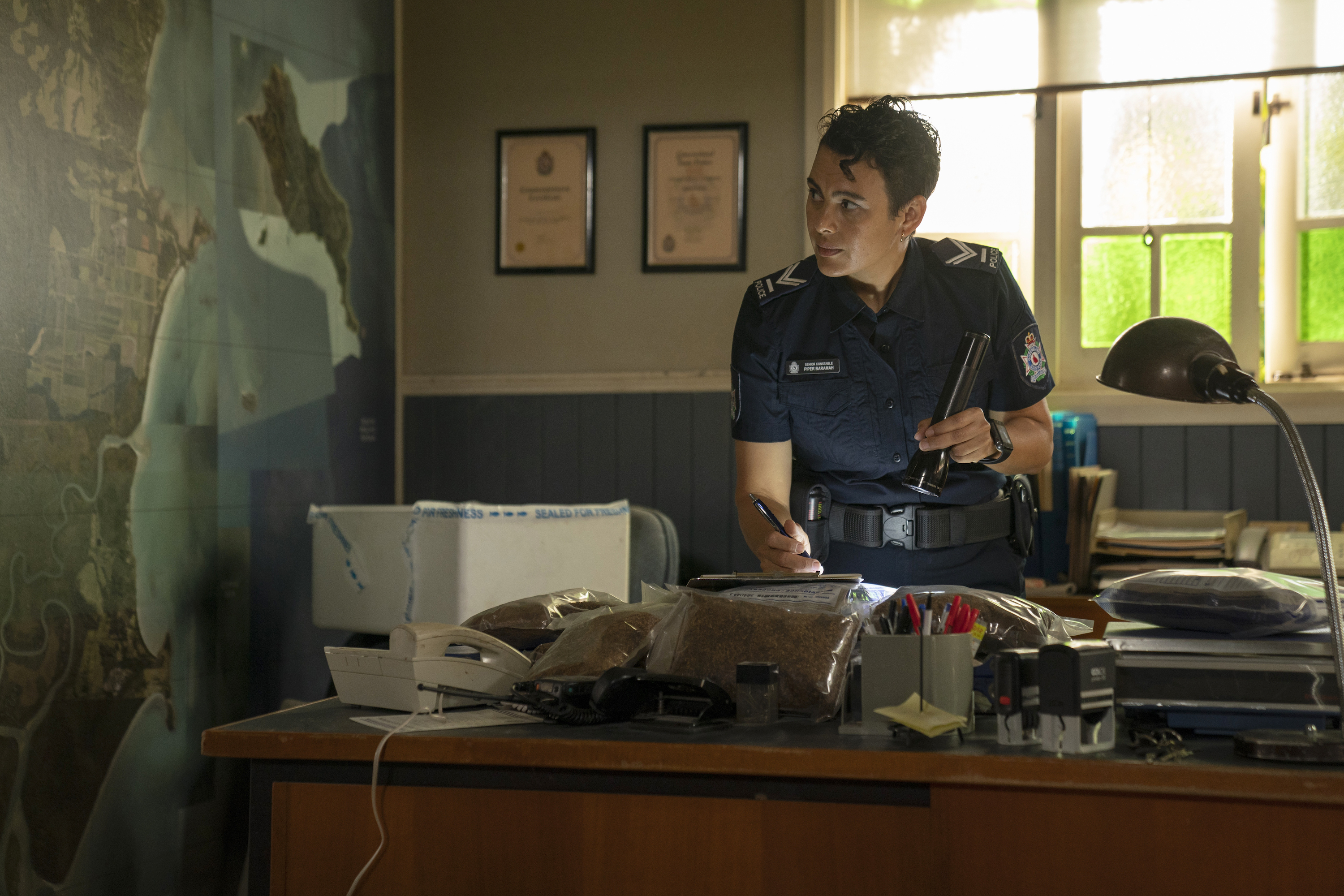 A cop uses a flash light at her desk in a scene from Irreverent.