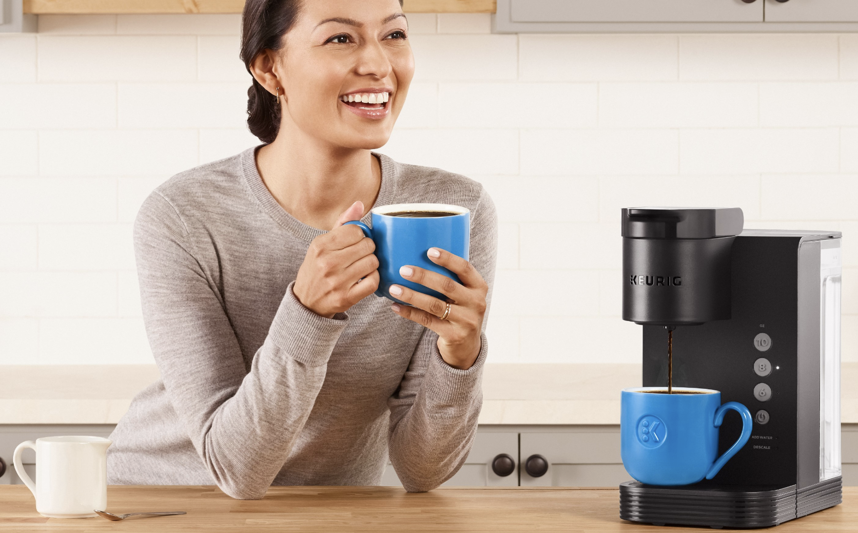 A woman sitting next to a Keurig K-Express coffee maker.