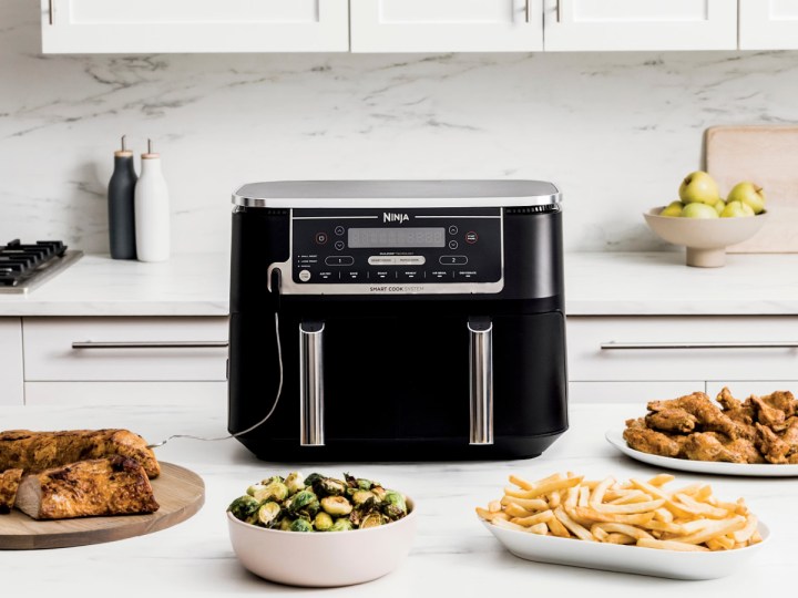 Ninja Foodi 6-in-1 10-quart XL 2-Basket Air Fryer on a white kitchen counter with a variety of air fried foods.