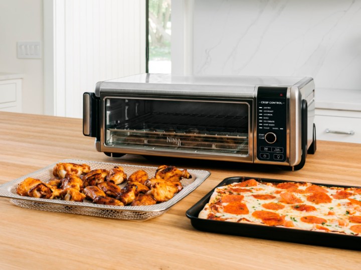 Ninja Foodi 8-in-1 Digital Air Fry Oven on a kitchen counter with pizza and wings.