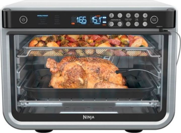 The Ninja Foodi oven with a whole chicken and a pan of vegetables inside it.