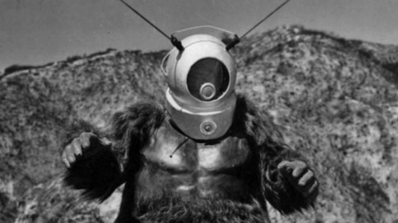 Ro-Man em um deserto com os braços levemente levantados no filme Robot Monster de 1953.