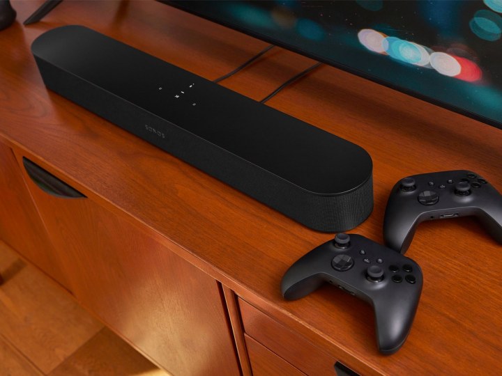 The Sonos Beam 2 soundbar on a media cabinet with a couple of video game controllers.