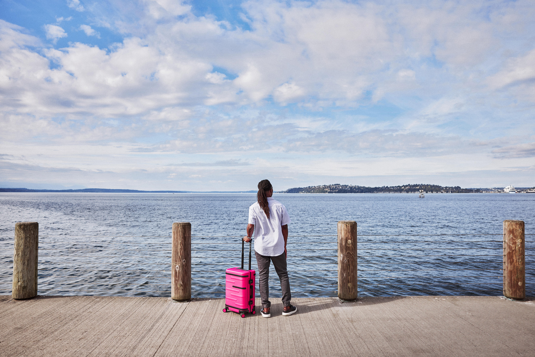 Una mujer de pie en el borde de un muelle con la maleta rosa brillante T-Mobile Un-carrier On.