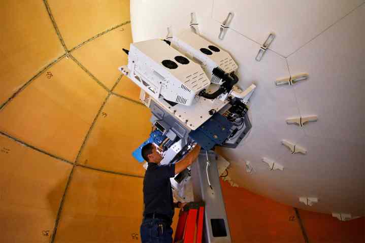 Tecnico in piedi sulla scala che lavora sul retro di una grande parabola satellitare.
