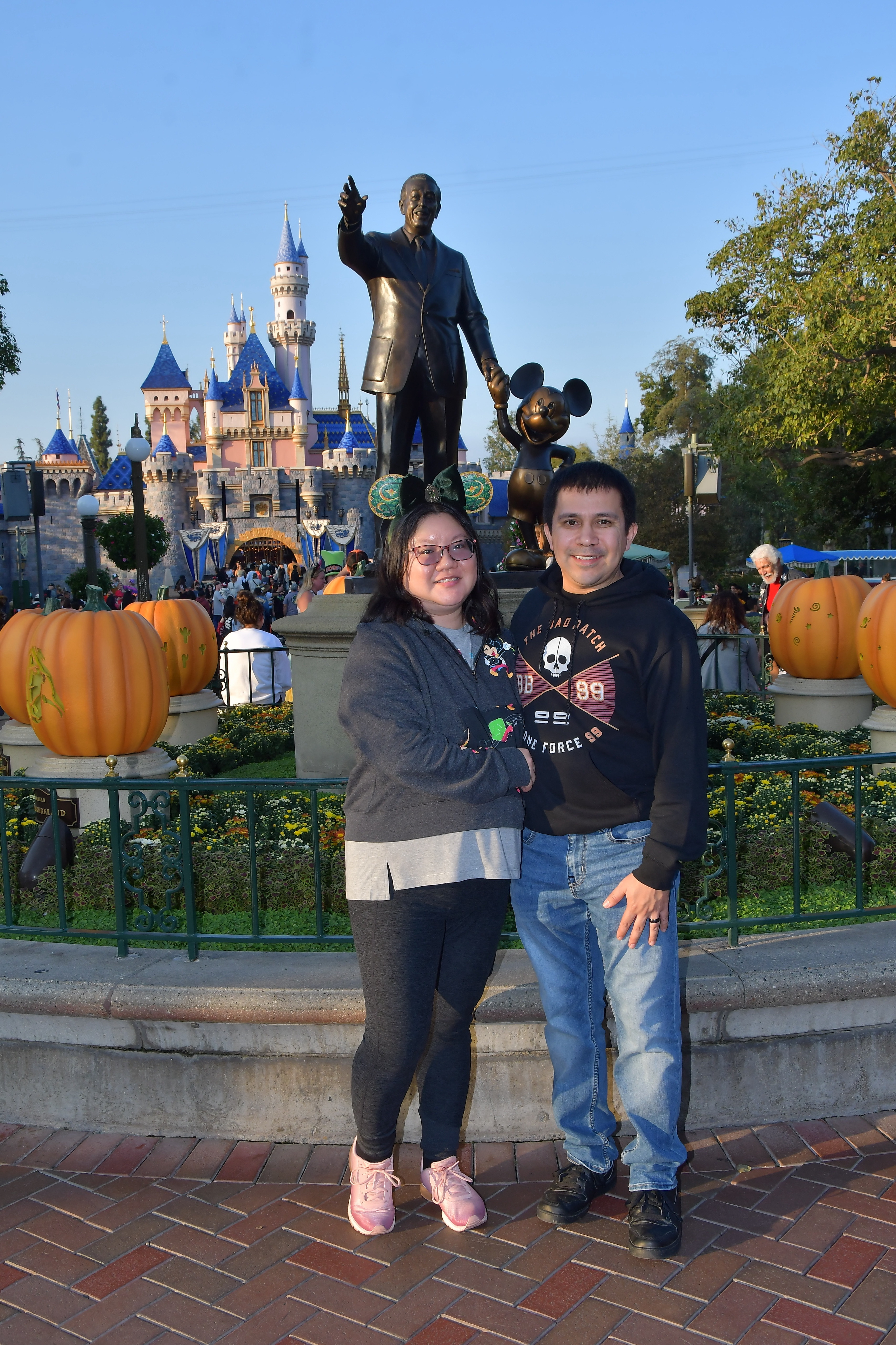 Christine e marido posam em frente à estátua de Walt Disney e Mickey Partner na Disneyland.