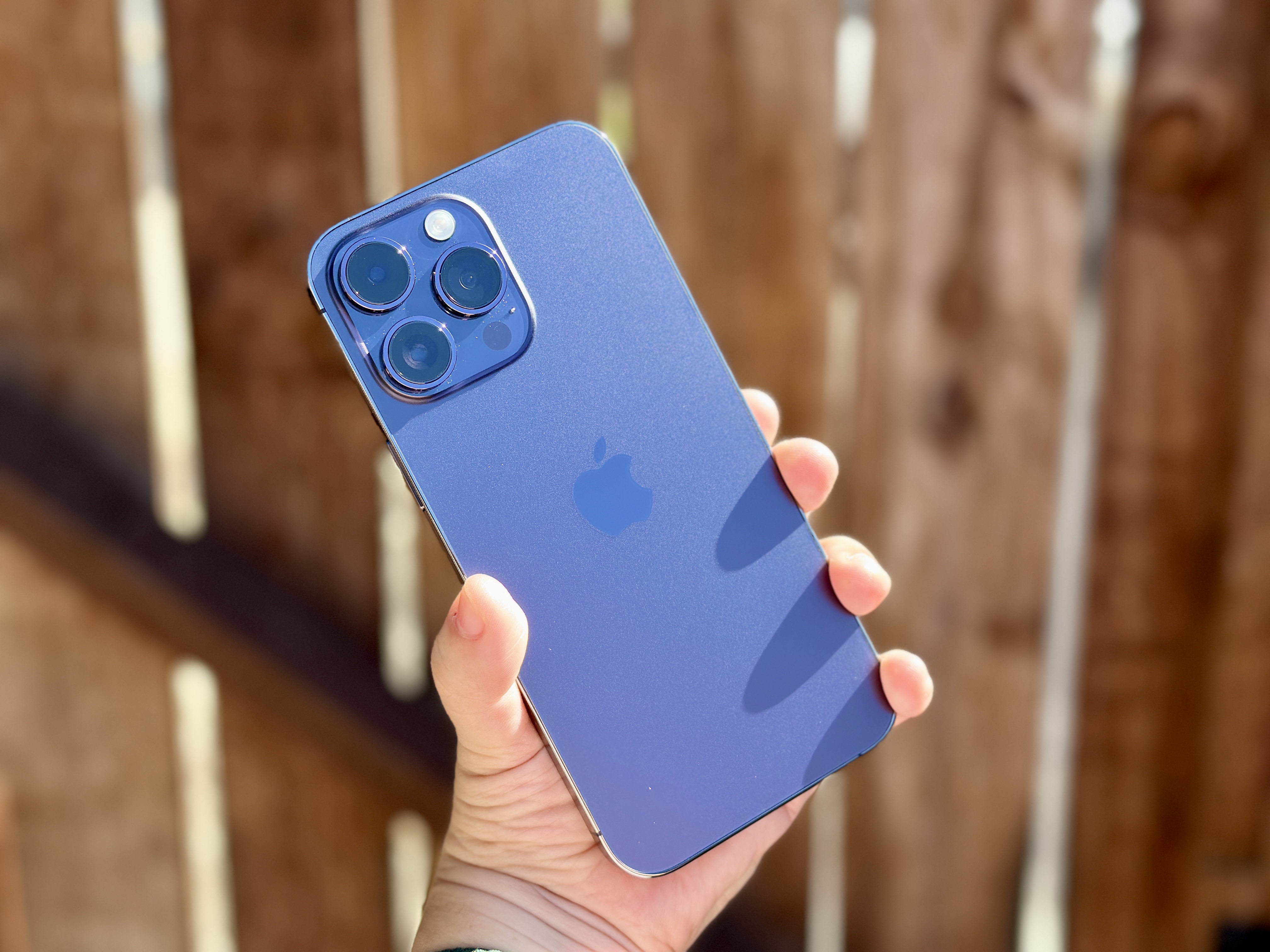 Deep Purple iPhone 14 Pro sostenido en la mano con una puerta de madera al fondo