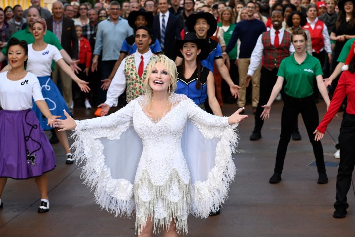 Dolly Parton canta con otras personas al aire libre en Dolly Parton's Mountain Magic Christmas.