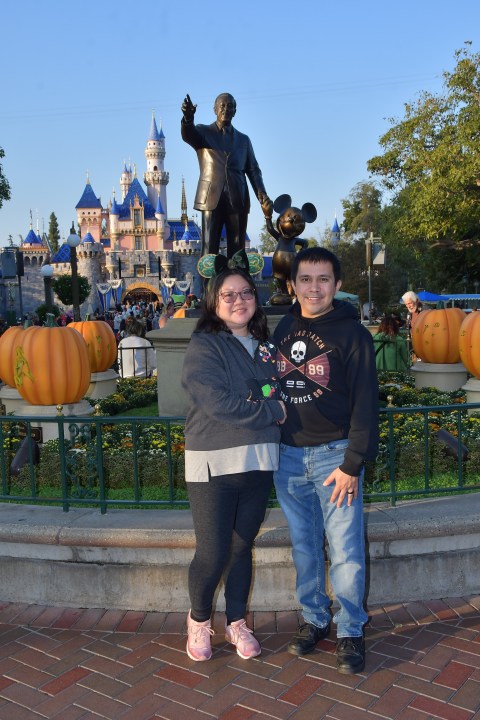 Christine and her husband pose at Disneyland's Walt and Mickey couple statue.