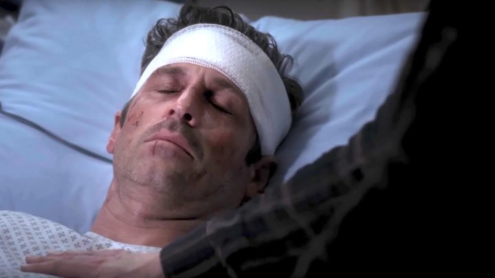 Dr. Derek Shepherd lying in a hospital bed, a bandage around his head in a scene from Grey's Anatomy.