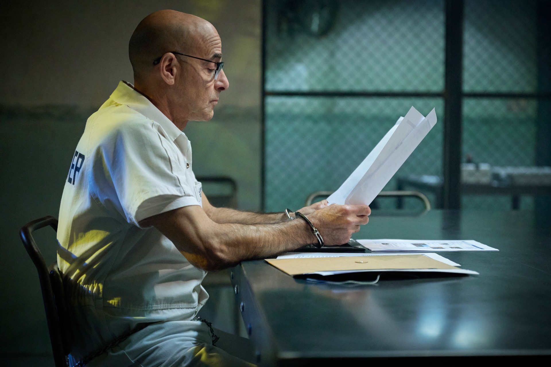 Un hombre está sentado en una mesa en la prisión en Inside Man.