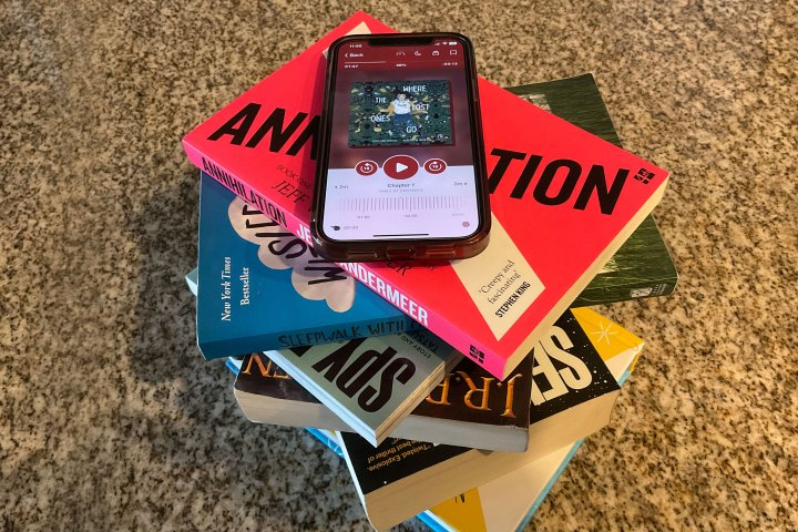 The Libby app that appears on the iPhone 12 sits on a tower of different books.