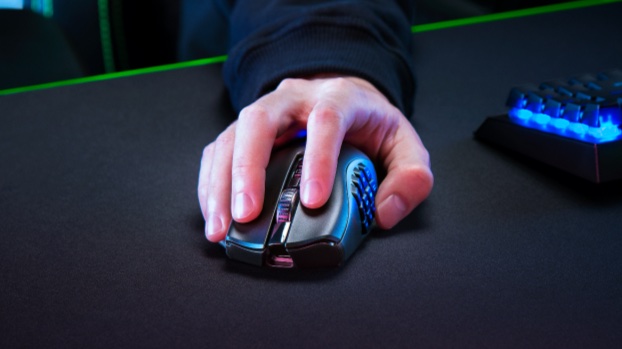 A man's hand holds a Naga 2 Pro gaming mouse on a black desktop