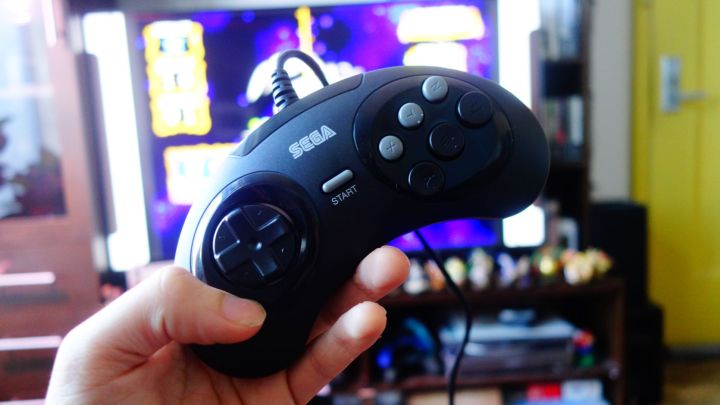 A Sega Genesis Mini controller held up in front of a TV.