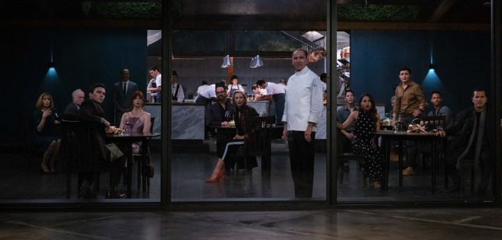 The chef and guests of a restaurant turn and look out the window in a scene from The Menu.