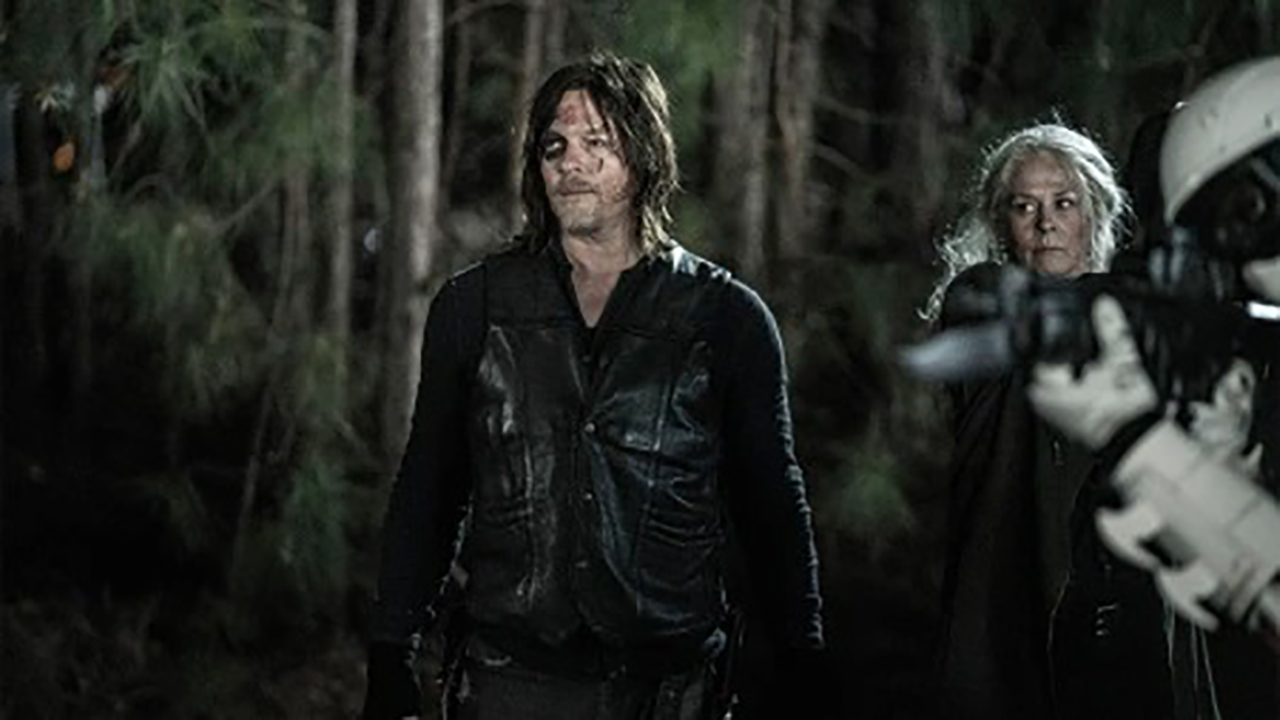 Daryl em pé, Carol ao fundo, em The Walking Dead.