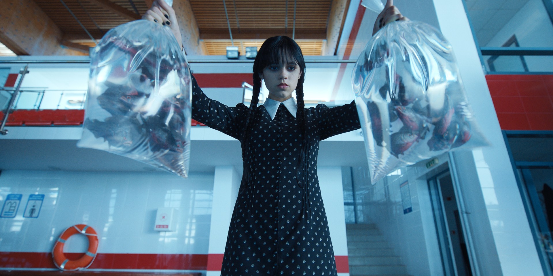 Jenna Ortega, as Wednesday Addams, holds two bags filled with piranhas.