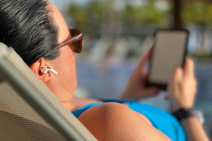 Donna in piscina con gli auricolari Apple AirPods e un e-reader.