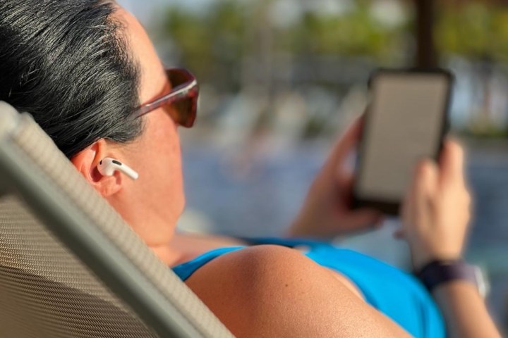 Woman by pool with Apple AirPods earbuds and an e-reader.