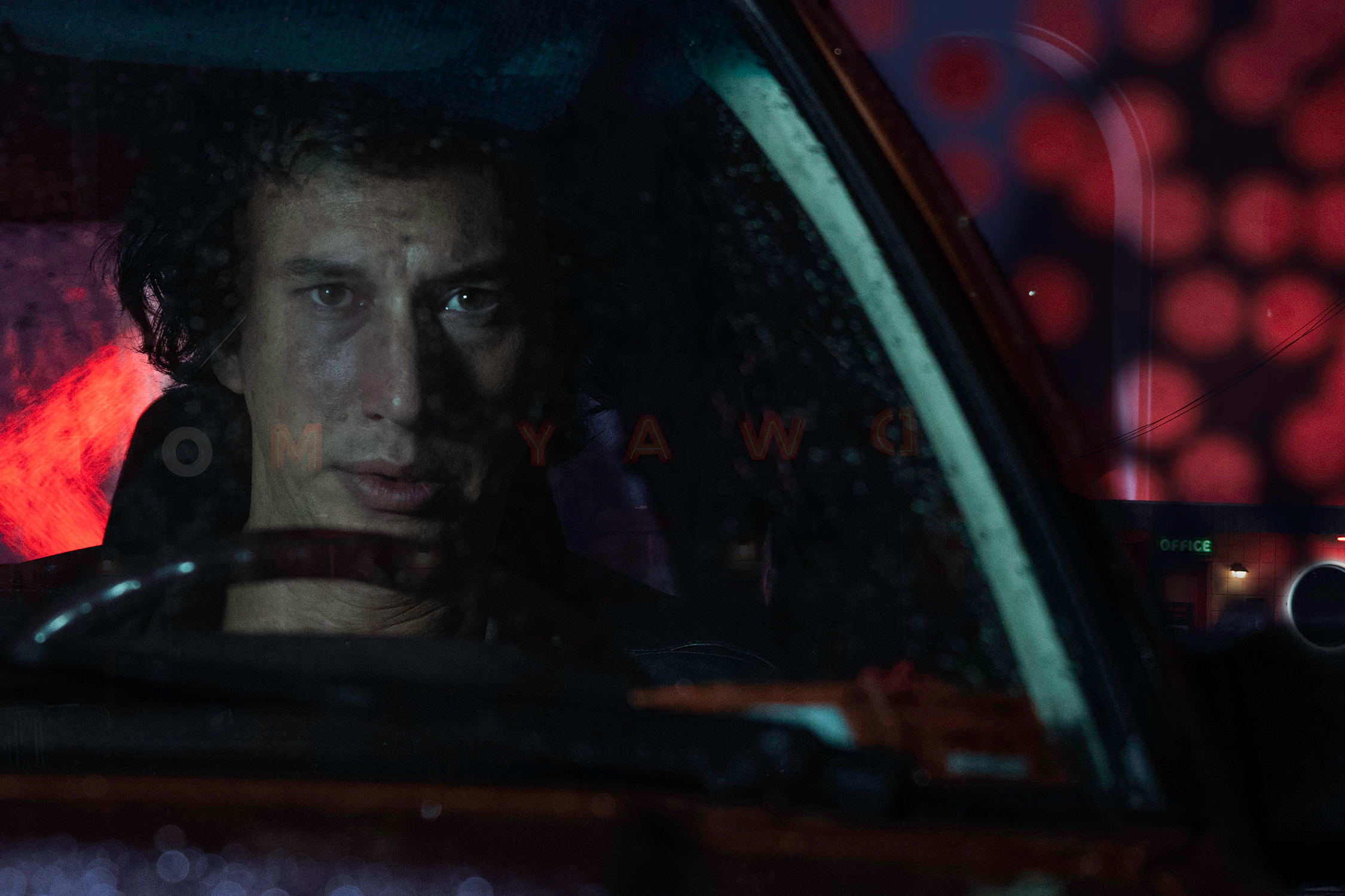 Adam Driver está sentado em um carro em White Noise, da Netflix.