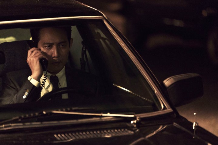 Lee Jung-jae holds a telephone while sitting in his car in Hunt.