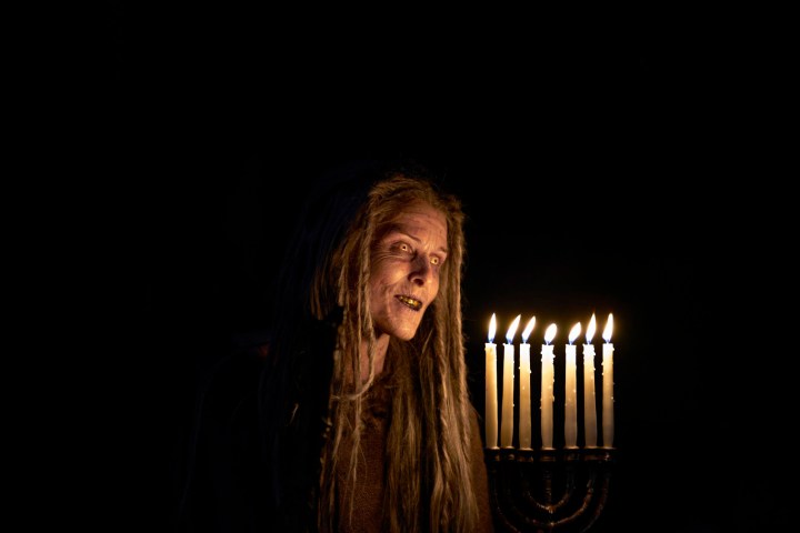 A creature holds a lit menorah n a scene from Lullaby.