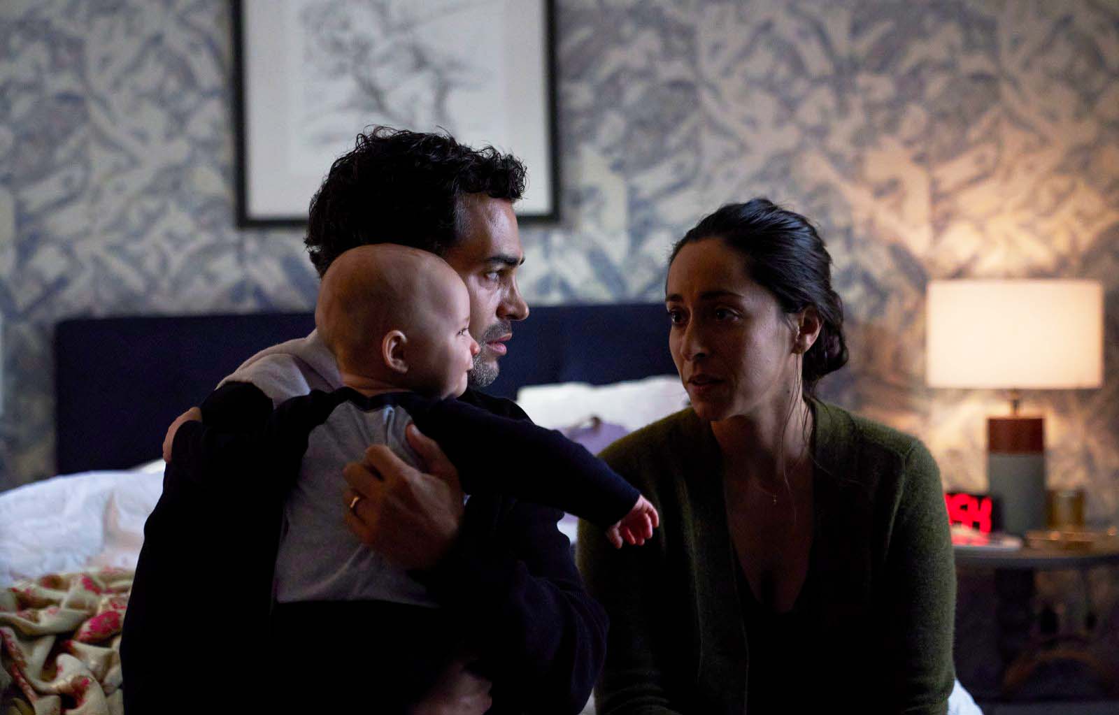 A man holds a baby while his wife looks at him in a scene from Lullaby.