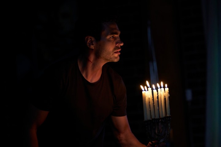 A man holds a menorah in a scene from Lullaby.