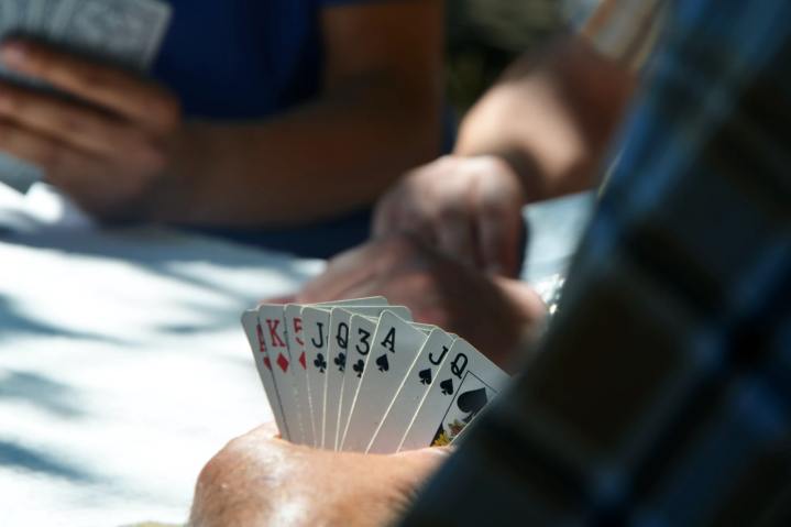 Des gens jouant aux cartes vus de dos, montrant la main d'un joueur.