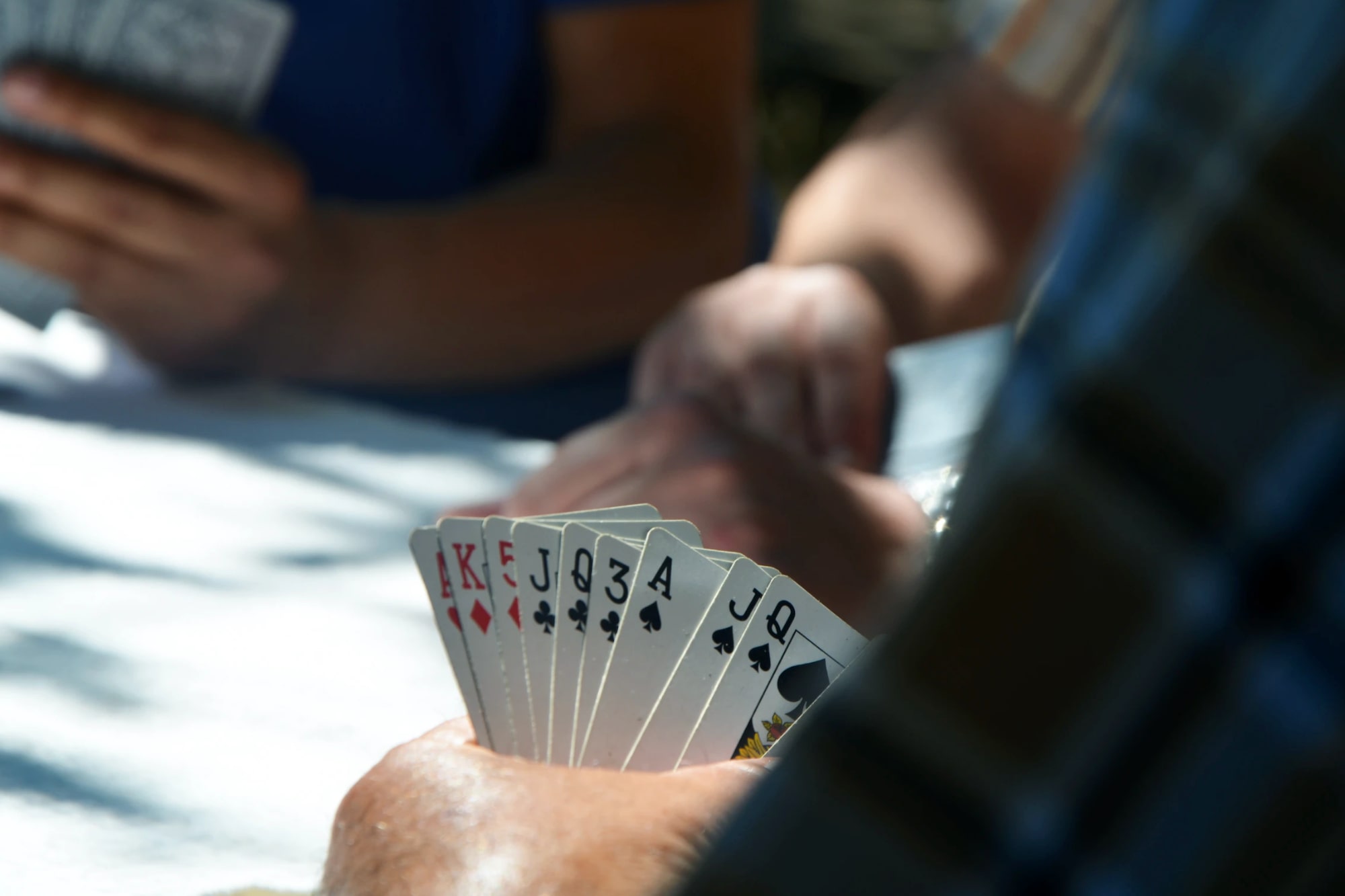 Personas jugando a las cartas vistas desde atrás, mostrando la mano de un jugador.