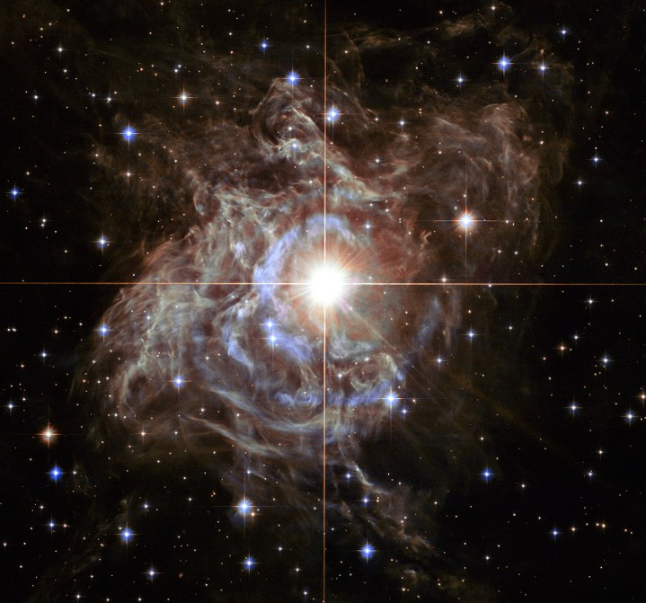 This festive NASA Hubble Space Telescope image resembles a holiday wreath made of sparkling lights. The bright southern hemisphere star RS Puppis, at the center of the image, is swaddled in a gossamer cocoon of reflective dust illuminated by the glittering star. The super star is ten times more massive than our Sun and 200 times larger.