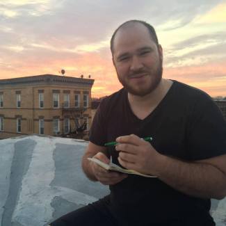 Andrew Thomas sits on a roof while sketching in a notepad.