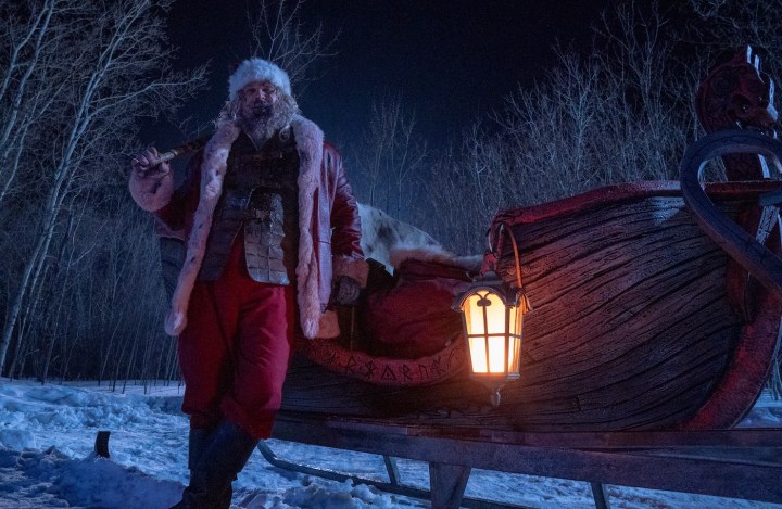 David Harbour, dressed as Santa Claus, leans against a sleigh.