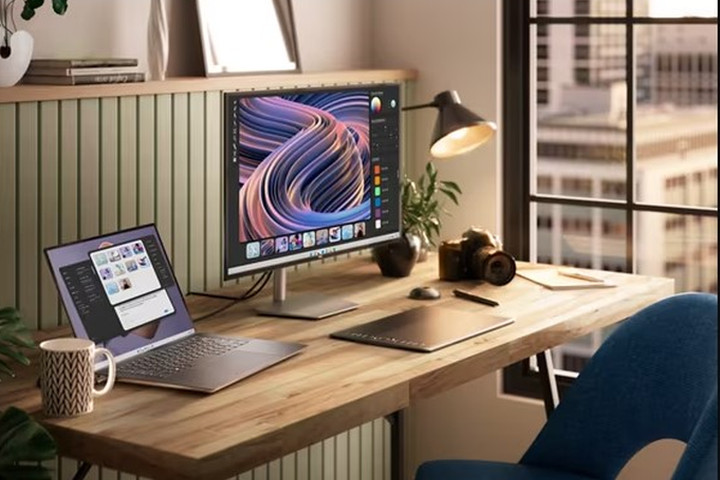 Um laptop Dell XPS 15 em uma mesa de escritório ao lado de um monitor.