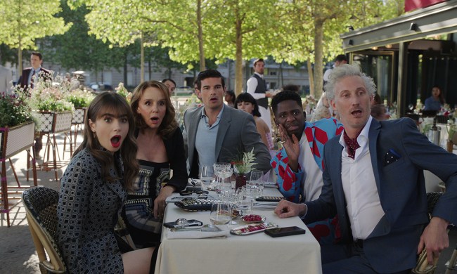 Emily, Sylvie, Nicholas, Julienne, and Luc sitting at a table outside, all looking shocked in a scene from Emily in Paris.