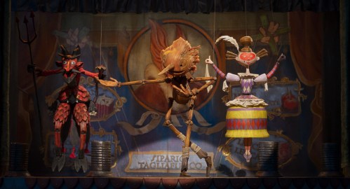 Pinocchio bows while performing on stage with several marionettes.