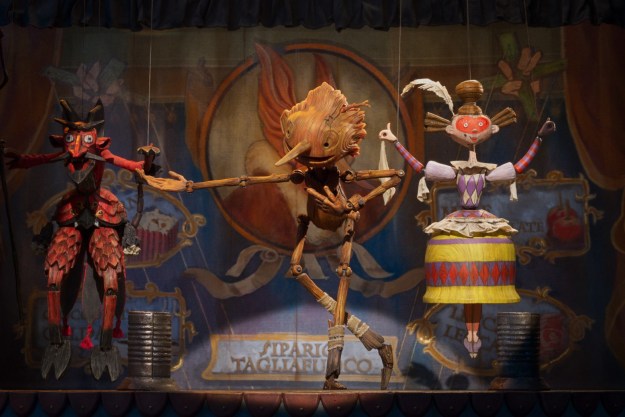 Pinocchio bows while performing on stage with several marionettes.
