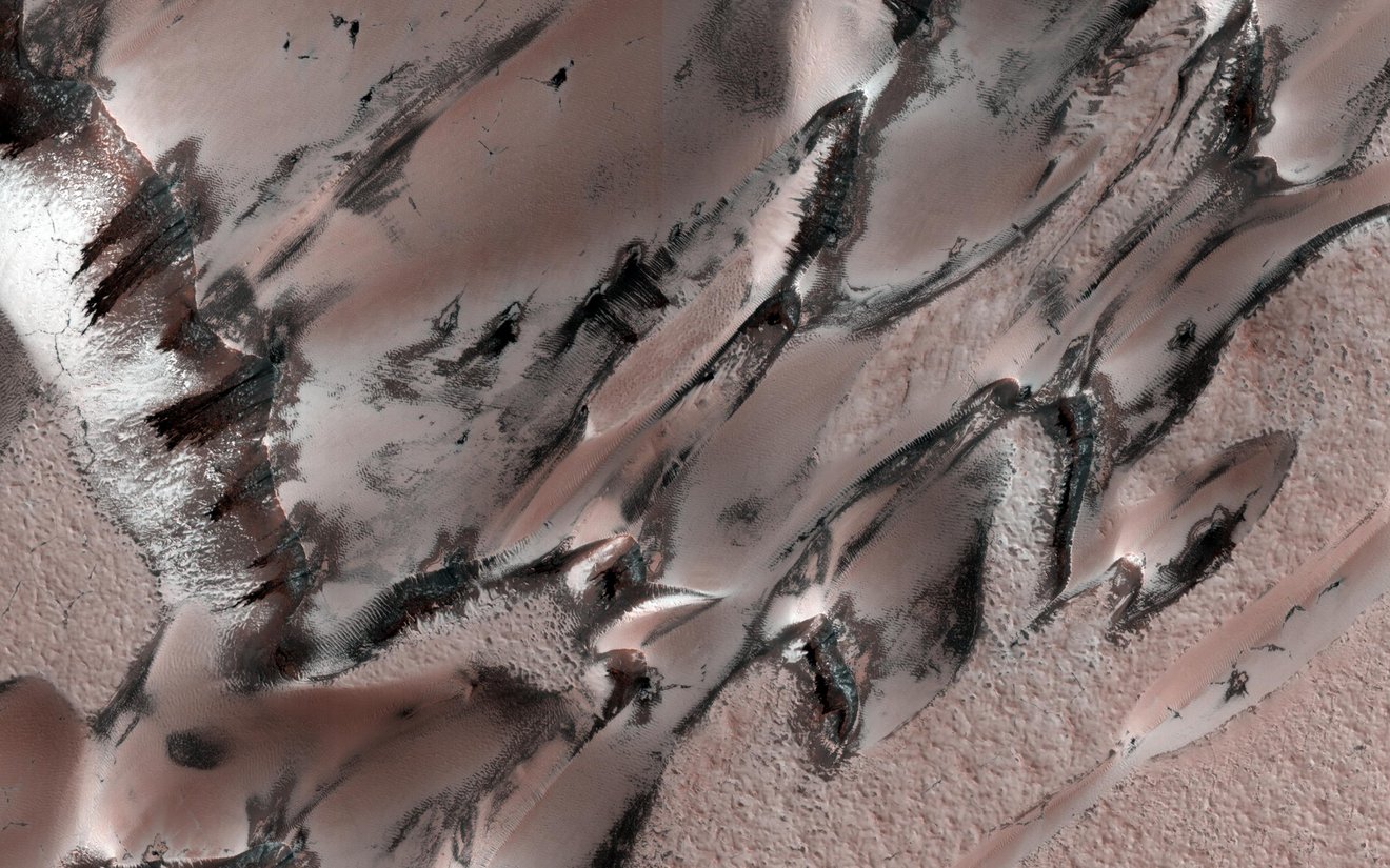 Dieses Bild, das am 22. Juli 2022 vom Mars Reconnaissance Orbiter der NASA aufgenommen wurde, zeigt Sanddünen, die sich über die Landschaft bewegen.  Winterfrost bedeckt die kältere, nach Norden gerichtete Hälfte jeder Düne.  Dieses Bild, das am 6. Mai 2021 vom Mars Reconnaissance Orbiter der NASA aufgenommen wurde, zeigt ein einzigartiges polares Dünenfeld im nördlichen Frühling, das einige interessante Muster enthüllt.  HiRISE hat diese „Megadünen“, auch Barchans genannt, eingefangen.  Über den Dünen haben sich im Winter Kohlendioxidfrost und -eis gebildet;  Wenn dieser im Frühjahr zu sublimieren beginnt, kommt der dunklere Dünensand zum Vorschein.