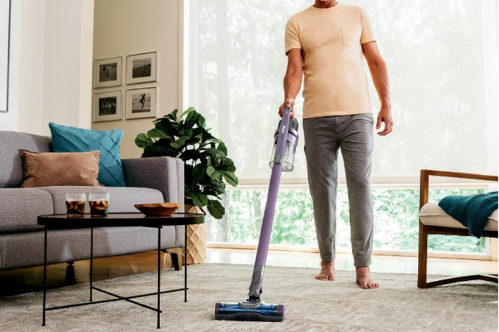 A man vacuums a rug with the Shark Pet Cordless Stick Vacuum.