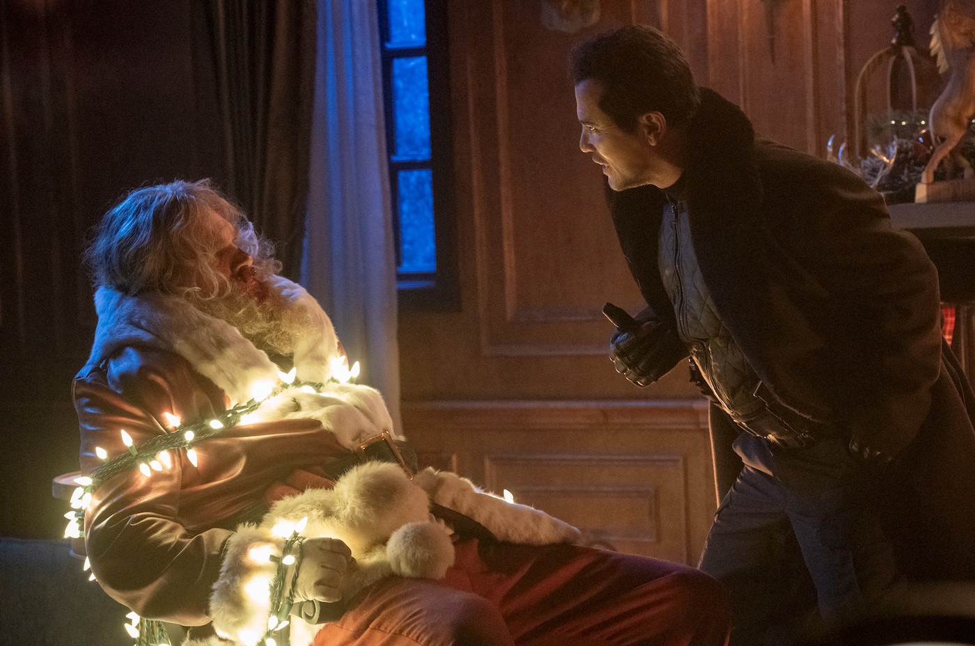 David Harbous disfrazado de Papá Noel y atado con luces navideñas, mientras John Leguizamo le grita.