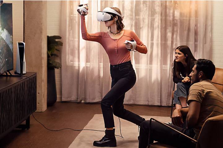A woman using Sony PlayStation VR 2 while friends watch on the TV.
