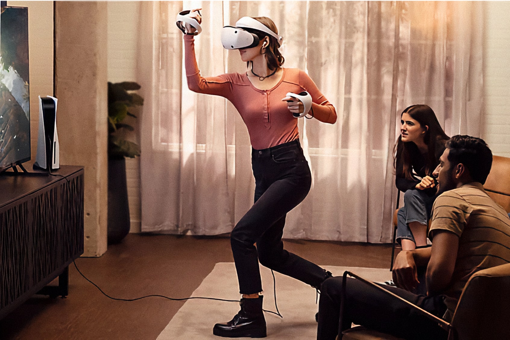 Uma mulher usando o Sony PlayStation VR 2 enquanto seus amigos assistem na TV.