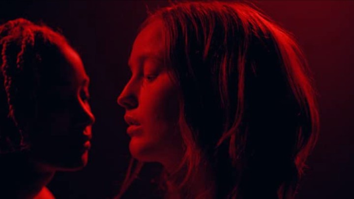 Two girls look at each other in red light in My Animal.